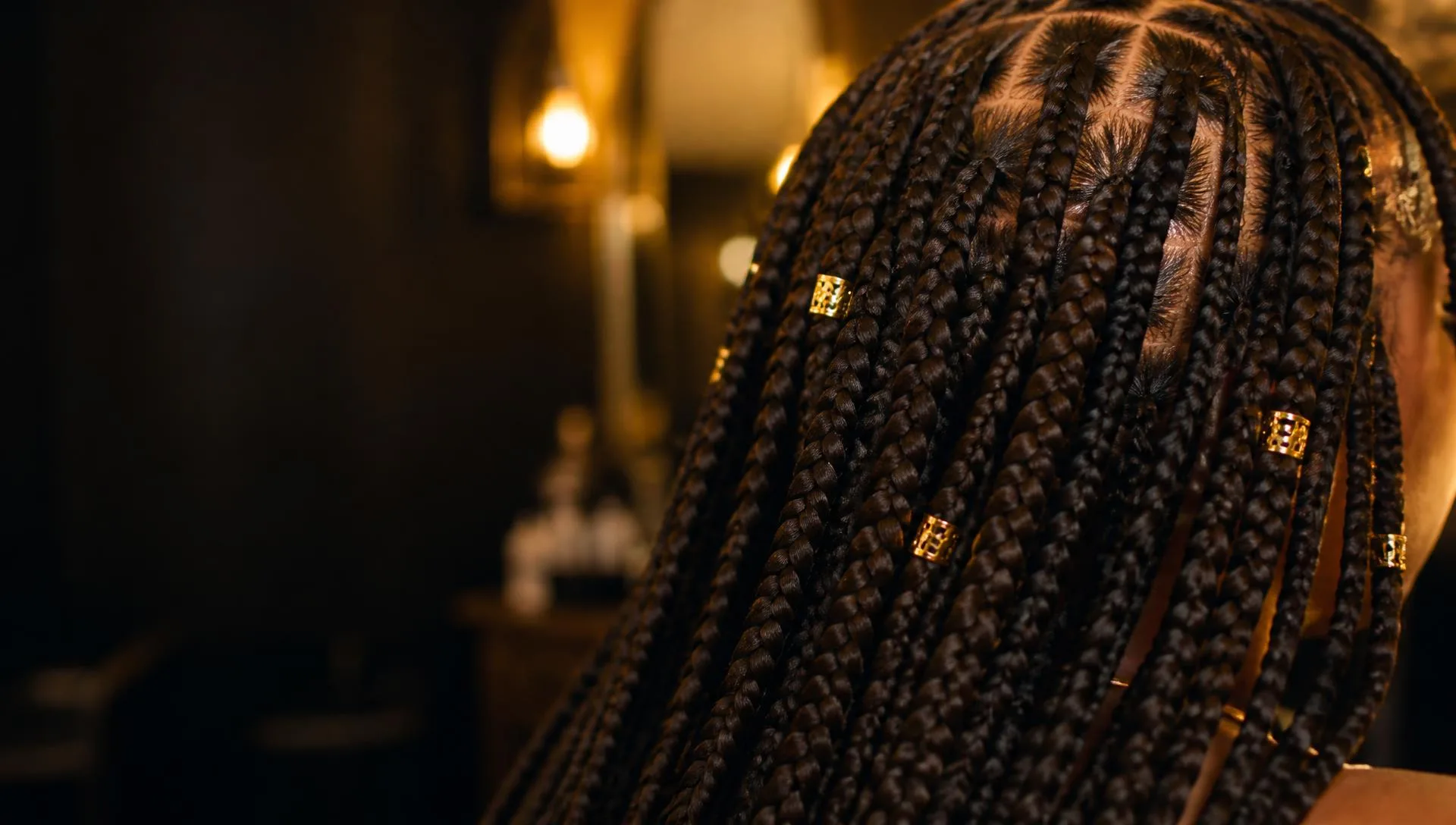 Long knotless braids finished with gold cuffs in warm salon light
